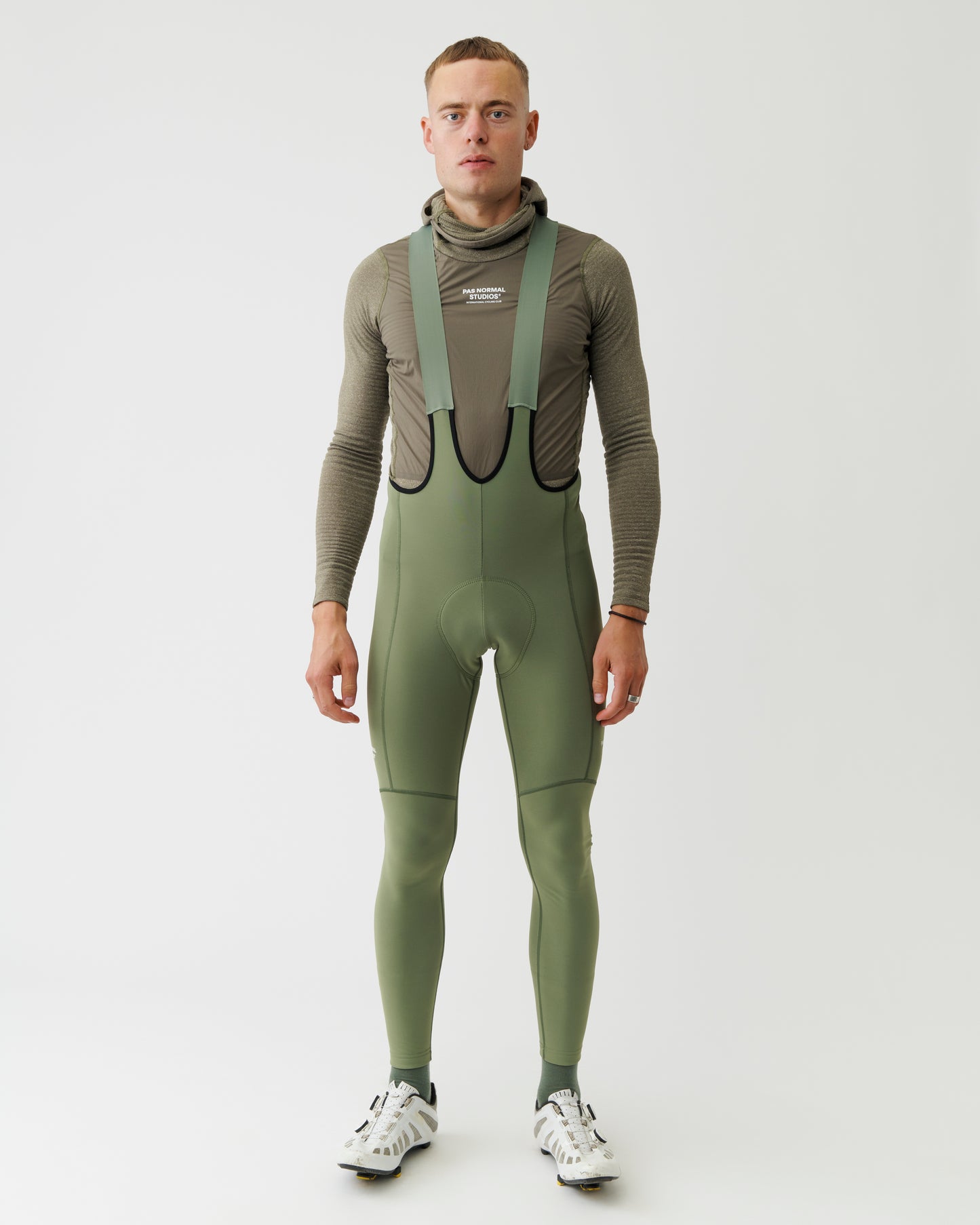 Person wearing a green ski suit with suspenders on a white background