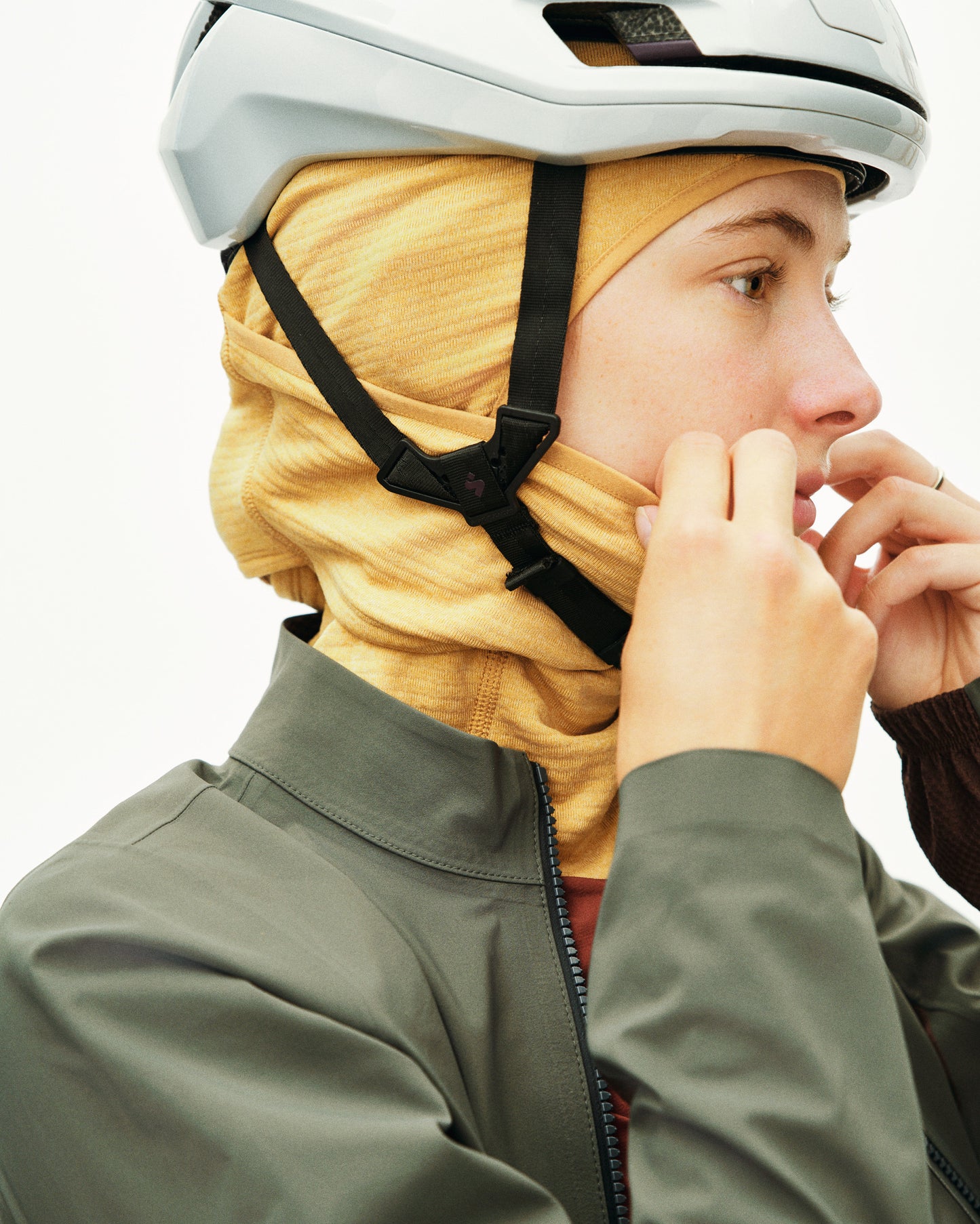 Person wearing a helmet and a yellow headscarf with a green jacket on a white background