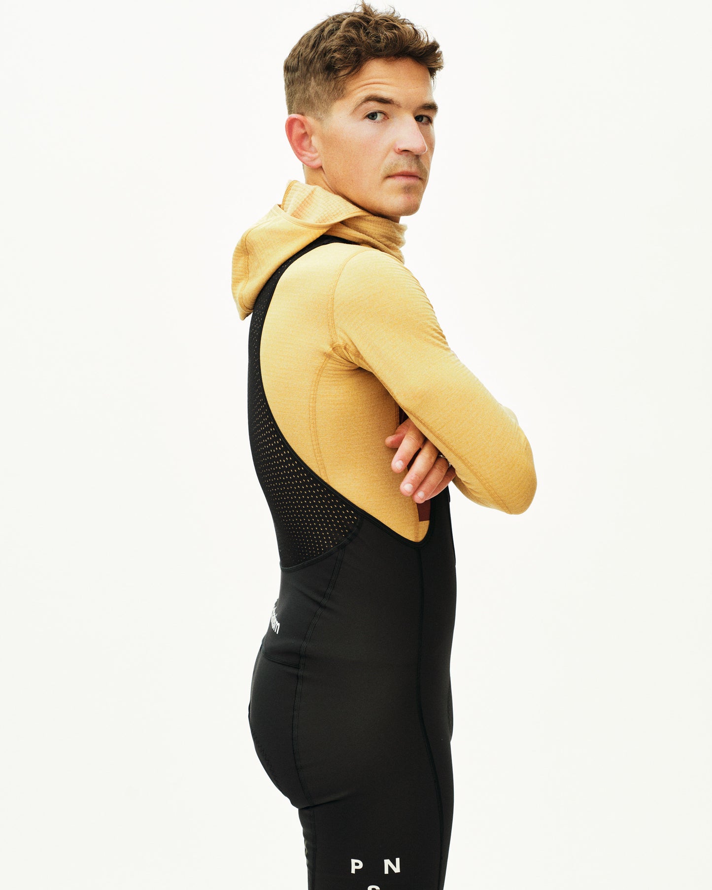 Man wearing a mustard yellow hoodie and black athletic outfit on a white background