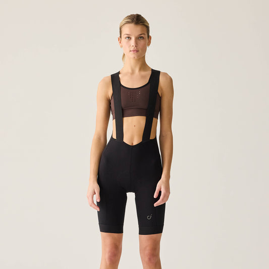 A woman wearing a sleeveless black bib short designed for cycling, with the brand logo visible on the fabric.