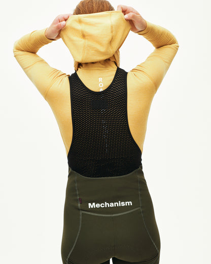 Person wearing a yellow hoodie, black back protector, and green Mechanism shorts on a white background