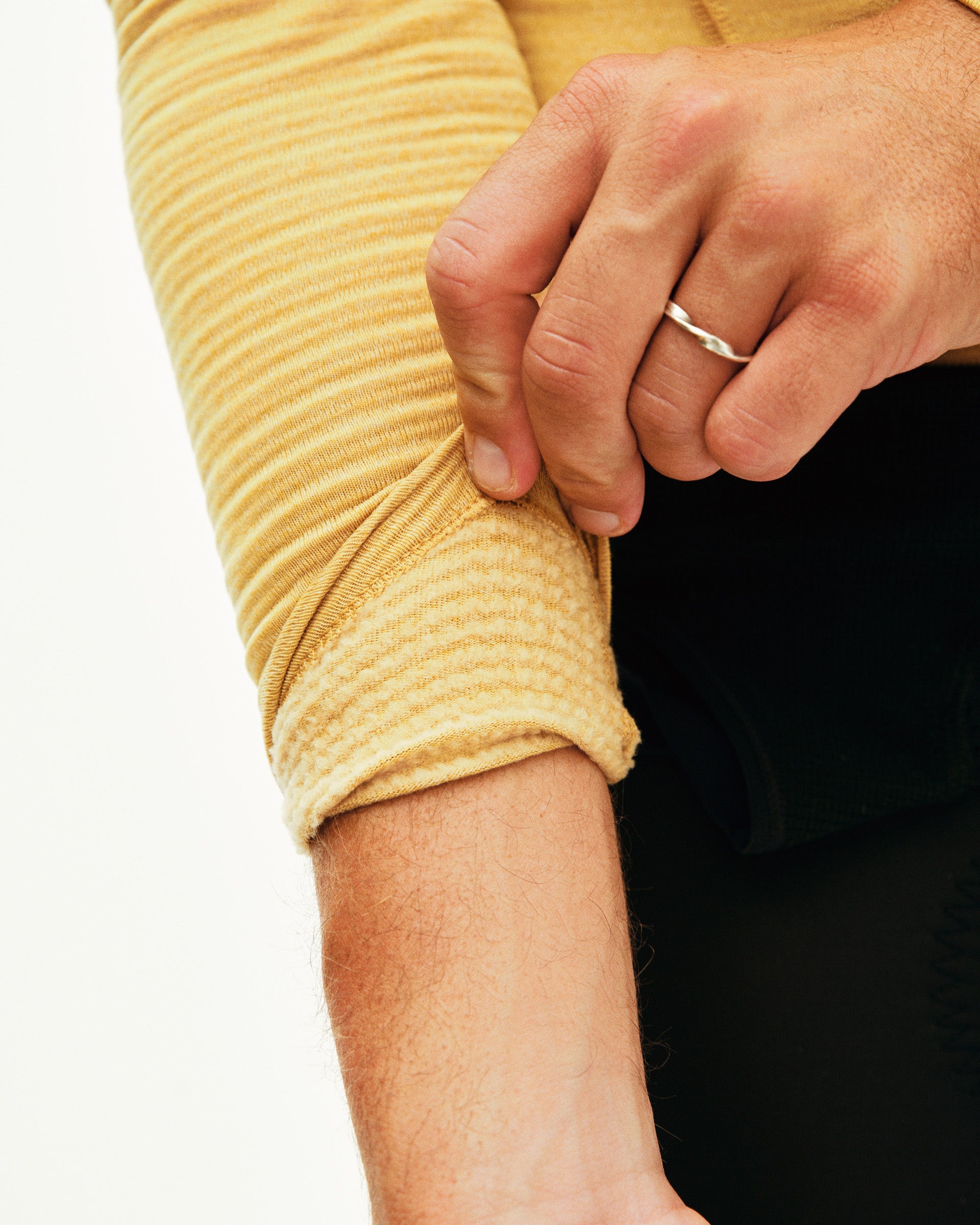 Close-up of a person wearing a yellow long-sleeve shirt with rolled-up sleeves.