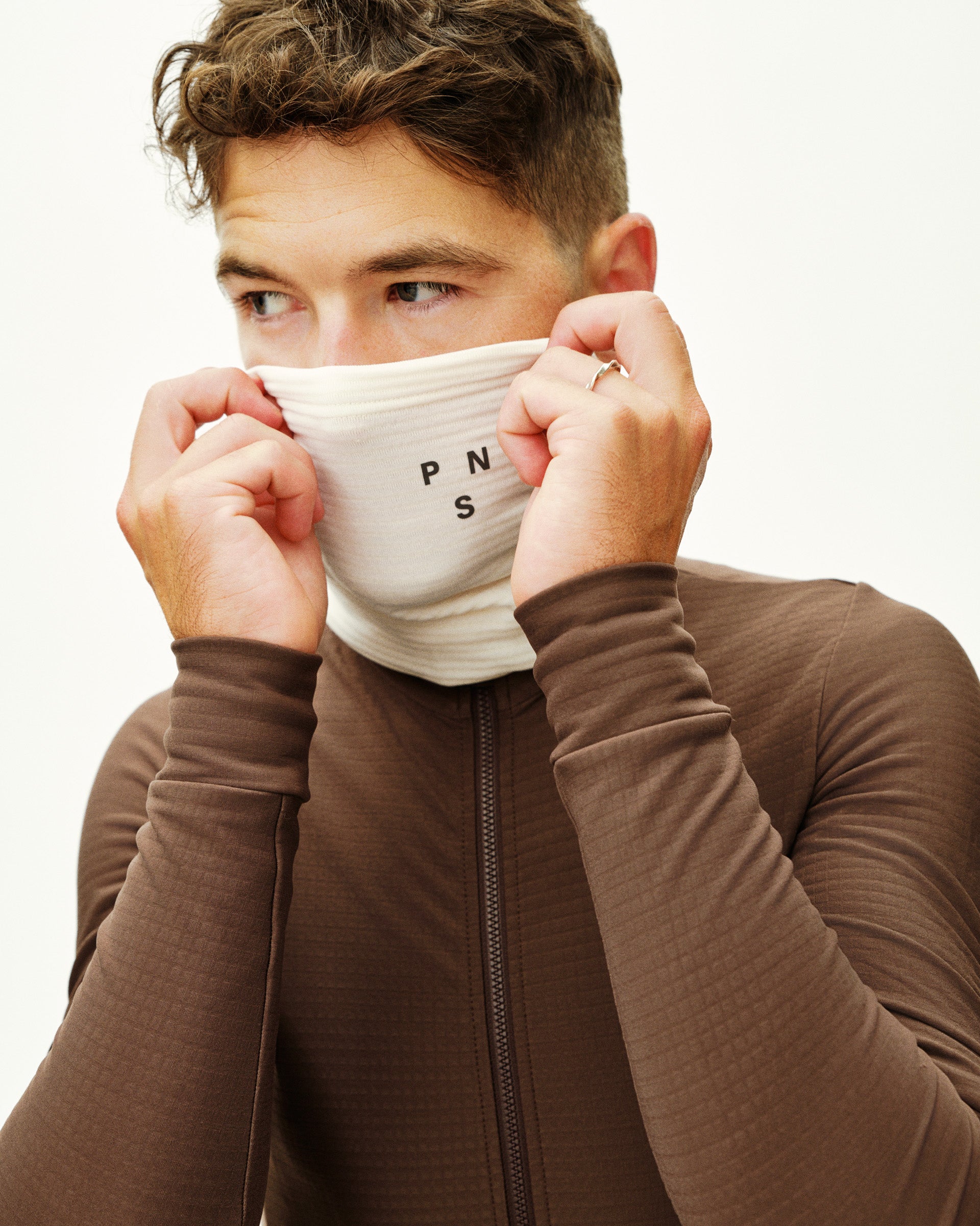 Person wearing a brown jacket with a white face mask covering their mouth and nose.
