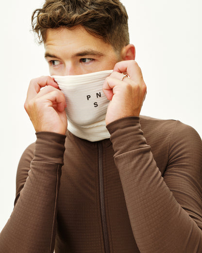 Person wearing a brown jacket with a white face mask covering their mouth and nose.