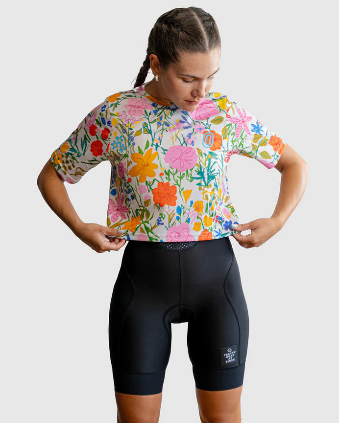 Person wearing a colorful floral cycling jersey and black shorts on a light gray background