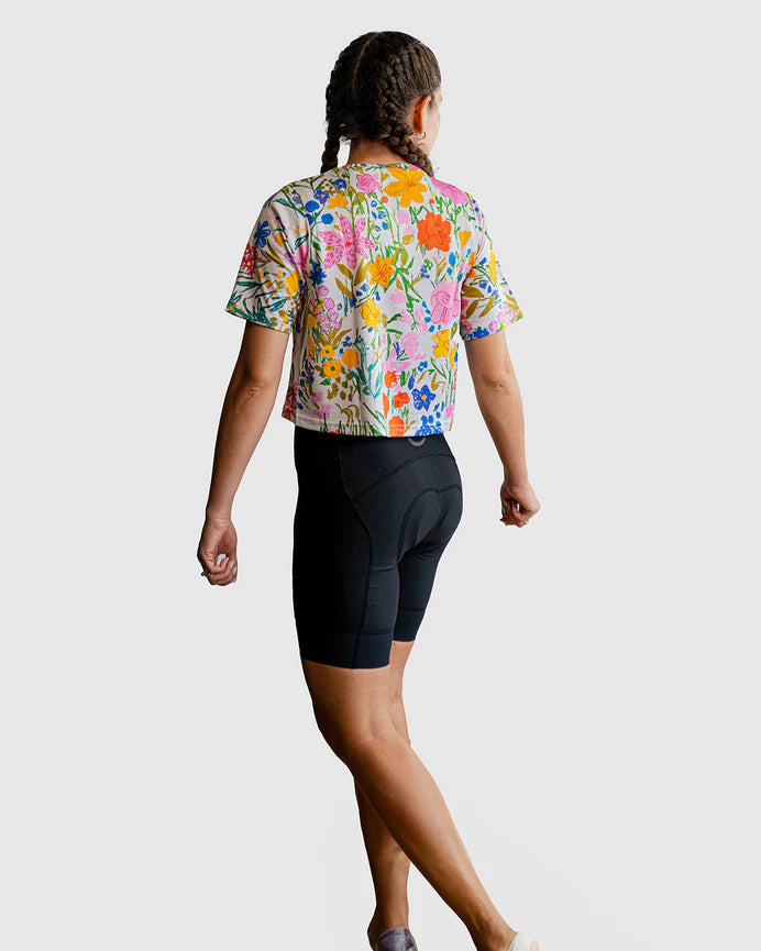 Person wearing a colorful floral cycling jersey and black shorts on a white background